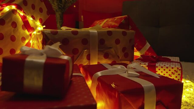 Decorated Christmas tree with lights, balls and presents. New Year's holiday atmosphere, winter fairy tale and Christmas spirit at home. Gift red packages with ribbons under a green tree. Slow motion.