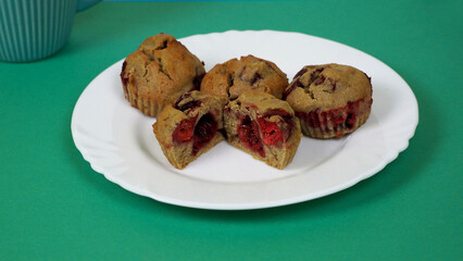 four muffins made from rice flour, yogurt, cherries and pumpkin oil, on a white plate on a green background, side view. gluten-free homemade cakes