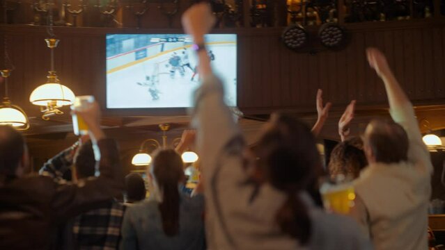 Group of Ice Hockey Fans Watching a Live Match Broadcast in a Sports Pub on TV. People Cheering, Supporting Their Team. Crowd Goes Ecstatic When Team Scores a Goal and Wins the Championship.
