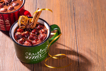 Homemade hazelnut  hot chocolate, dark winter cocoa drink with a lot of nuts, chocolate and spices, in cozy winter Christmas red and green cups, with Xmas New Year decorated background copy space