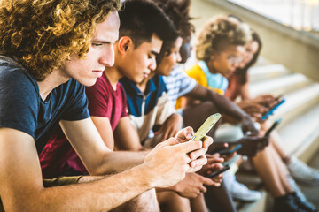 Group of young people using smart mobile phone device together - University students sitting in...