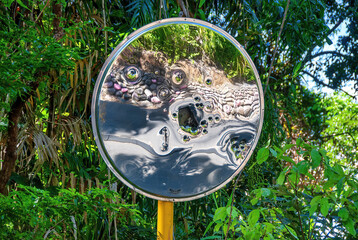 Mirror at a road crossing ruined by small holes. Ruined spherical road mirror at the intersection of roads in the forest against the background of green trees