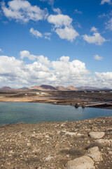 Obraz premium Deserted landscape of some old salt pans. salt pans constructions. Calm ocean. mountains in the background. Clear sky with big white fluffy clouds. Sand and rocks. Lanzarote, Canary Islands, Spain.