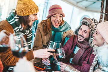 Happy friends group toasting red wine dining at restaurant terrace - Young people socializing drinking and eating food sitting outside at winery bar table - Winter season - Dinner lifestyle concept