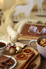 Cup of tea or coffee, various sweets and spices, Christmas decorations, comfy blanket, books and glasses. Selective focus.