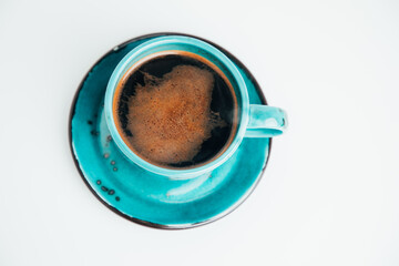 Blue mug with black coffee with a saucer on a white table. Top view, close-up