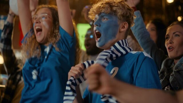 Group of Soccer Fans with Painted Faces Cheering, Screaming, Raising Hands and Jumping During a Football Game Live Broadcast in a Sports Pub. Player Scores a Goal and Friends Celebrate. Slow Motion.