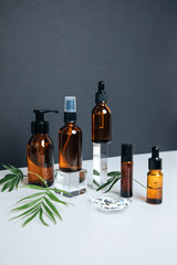Amber bottles with facial treatment on a glass cube with a branch of deer palm on the black background. Front view