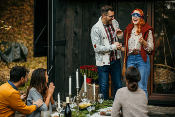 Host couple having a toast and surprising their group of friends at a garden party with positive news. The redhead woman is having a blindfold and the man is surprising her