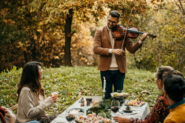 A handsome man plays the violin at a small wedding party while people are eating, clapping, and...