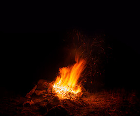 Open fire fireplace outdoor forest. Burning wood at night. Campfire at touristic camp at nature in mountains. Flame and fire sparks on dark abstract background. Burning sparks flying