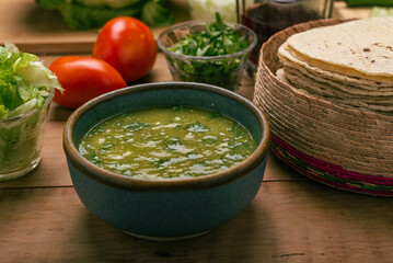 Tortillas, bowl with green sauce and vegetables on a wooden table. Typical Mexican food.