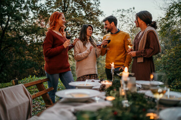 Group of elegantly dressed friends having a small boho dinner/wedding outdoors in a garden, drinking wine and talking to each other with a great mood and smiles. Man talking with a three females.