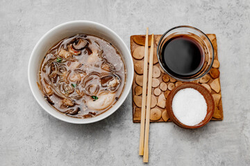 Udon soup with shrimps and a bowl with soy sauce on a gray background. View from above.
