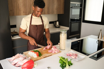Young african man de-boning chicken to prepare a recipe in a kitchen.