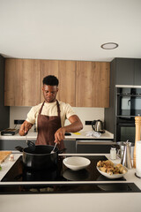 Fototapeta na wymiar Young african man preparing fried chicken mince with vegetables recipe in a kitchen.