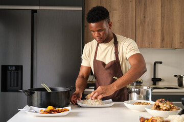Fototapeta na wymiar Young black man serving fried chicken mince on rice on a plate in a kitchen.
