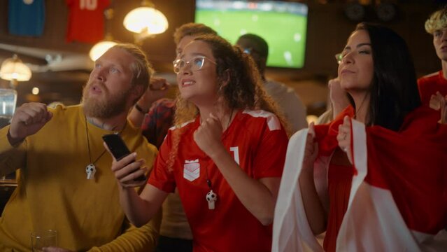 Portrait of an Anxious Multiethnic Female in Red Jersey Holding a Smartphone, Nervous About the Sports Bet on Her Favorite Soccer Team. Happy Victorious Emotions When Football Team Scores a Goal.
