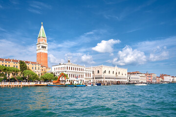 Fototapeta na wymiar Doge's palace and Campanile on Piazza di San Marco, Venice, Italy with sea water on foreground. Calm sunny day in Summer, blue sky with clouds.