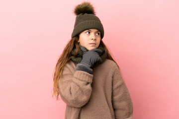 Little girl with winter hat isolated on pink background having doubts