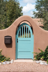 Turquoise colored gate in an arched entrance to a garden in an adobe wall in Santa Fe, New Mexico
