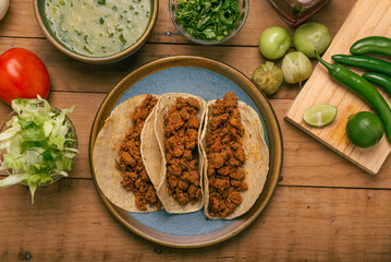 Marinated beef tacos, bowl with salsa verde and vegetables on a wooden table. Tacos de adobada.