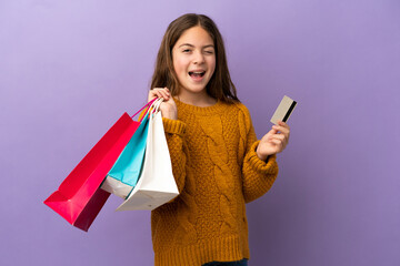 Little caucasian girl isolated on purple background holding shopping bags and a credit card