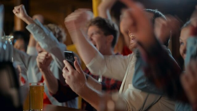 Portrait of an Excited Young Man Sitting at Bar Counter, Drinking Beer and Using a Smartphone, Anxious About a Sports Bet on His Favorite Soccer Team. Joyful Emotions When Football Team Scores a Goal.