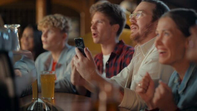 Excited Man in Glasses Sitting at a Bar Stand, Using a Smartphone, Feeling Alive After Putting a Bet on His Favorite Soccer Team. Ecstatic When Football Team Scores a Goal and He Wins the Prize.