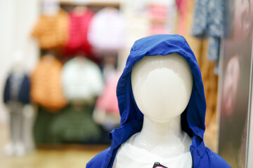 Closeup clear face without hair of boy mannequins wearing the childhood clothes design with blurred background of the shop and blurred foreground of another mannequin.