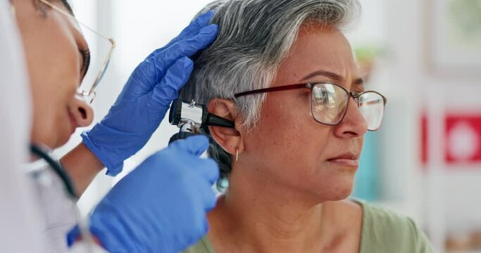 Doctor, elderly patient and ear exam, test or medical checkup for hearing aid or diagnosis at the hospital. Hands of audiologist with otoscope helping senior woman for audiology healthcare at clinic