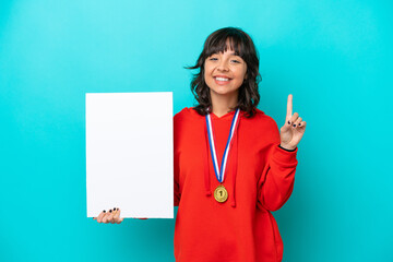 Young latin woman with medals isolated on blue background holding an empty placard and pointing up