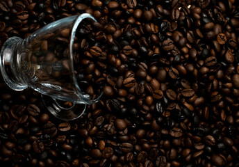 Taza de café acostada sobre una base de granos de café puros.
Fotografia oscura.