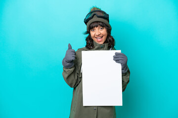 Skier latin woman with snowboarding glasses isolated on blue background holding an empty placard with thumb up