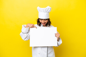 Young chef latin woman isolated on yellow background holding an empty placard with happy expression and pointing it