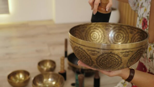Female hands is making sound, vibration from a Tibetan bowl, copy space. Buddhist music therapy, ritual closeup
