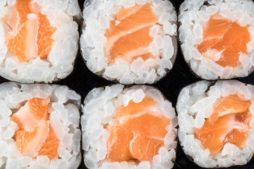 Macro top view of 6 salmon makis lined up on a black background.Take away. Oriental, Japanese food. Copy space.