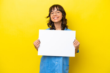 Fototapeta na wymiar Young nurse doctor woman isolated on yellow background holding an empty placard with happy expression