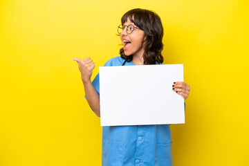 Young nurse doctor woman isolated on yellow background holding an empty placard and pointing side