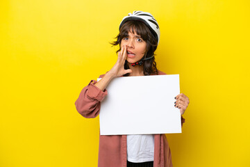 Young cyclist latin woman isolated on yellow background holding an empty placard and shouting