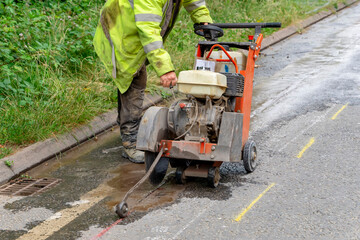 Builder using petrol powered road saw with dimond blade to cut asphalte road surface