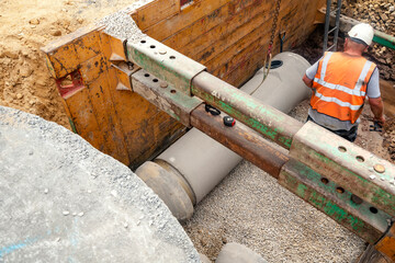 Builder installing big diameter concrete drainage pipe protected by trench support system during...