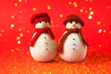 Two knitted snowmen on a red background in red and brown hats. Merry Christmas and New Year 2023 greeting card
