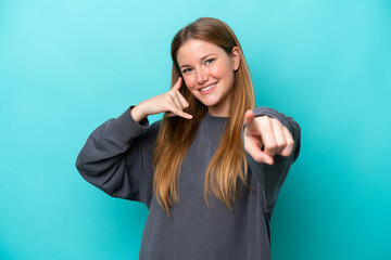 Young caucasian woman isolated on blue background making phone gesture and pointing front