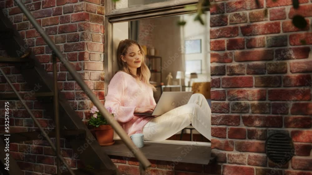 Aufkleber young caucasian woman working from home and using laptop while sitting on bedroom windowsill on a wa