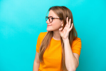 Young caucasian woman isolated on blue background listening to something by putting hand on the ear