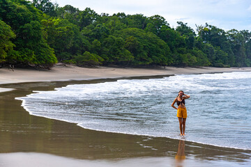 A beautiful girl in yellow shorts walks on a tropical beach with palm trees in manuel antonio national park in quepos, Costa Rica; tropical paradise beach in Costa Rica