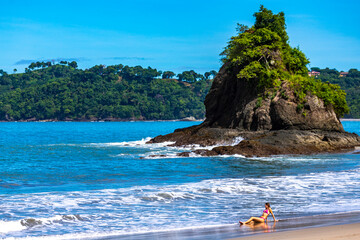 A beautiful girl in a pink bikini swims in the ocean on a tropical beach with little island  and palm trees in manuel antonio national park in quepos, Costa Rica; tropical paradise beach