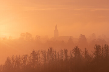 Aerial view of a church with trees in the foreground in the warm tones of sunset in Germany, dramatic sky