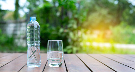 Drink water in bottle and glass over sunlight and natural green background.Select focus blurred...